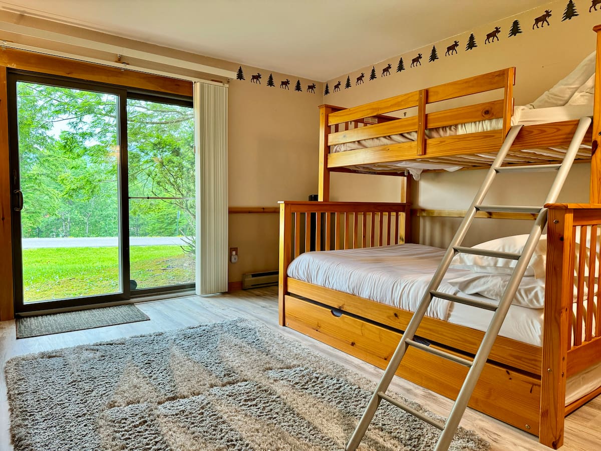 Bunk room with a pine bunk bed and trundle, a moose wallpaper border, and a sliding door to the lawn